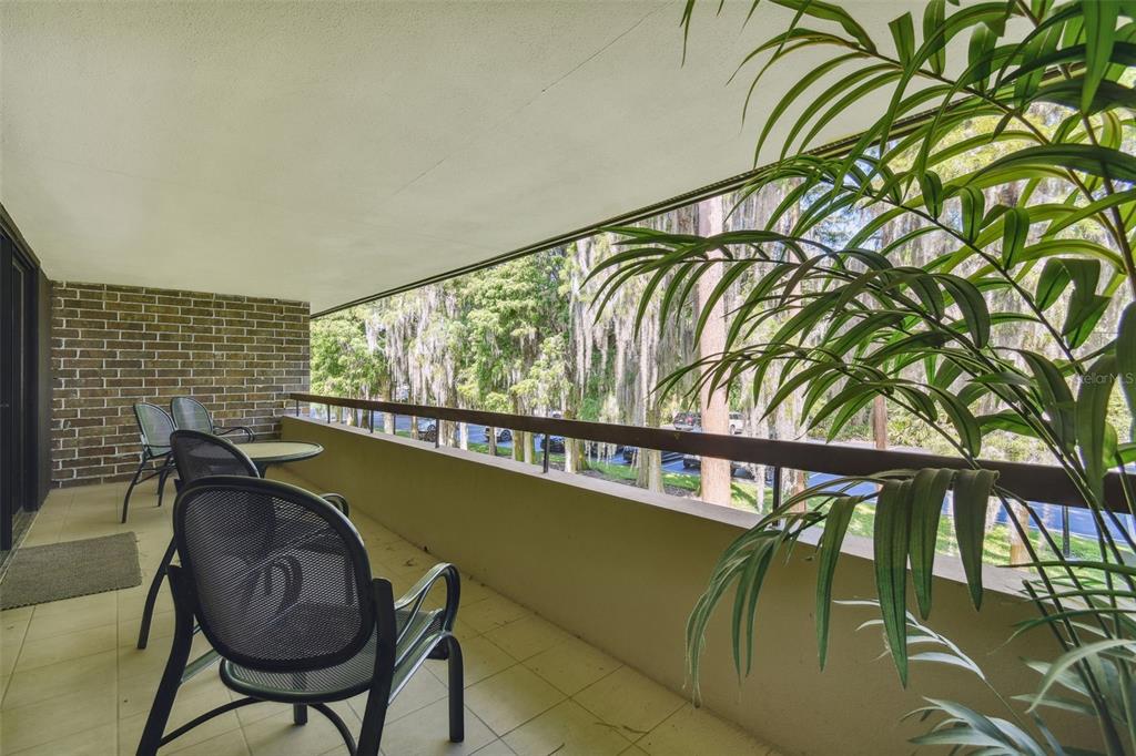 A balcony with a brick wall, patio furniture, and a view of trees and parking — 36750 US HIGHWAY 19 N UNIT 04239, PALM HARBOR, FL