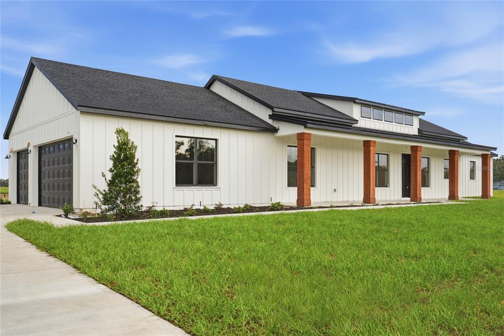 A white modern farmhouse with vertical siding, a dark roof, and wooden porch columns — 3890 SE 139 TERRACE, MORRISTON, FL