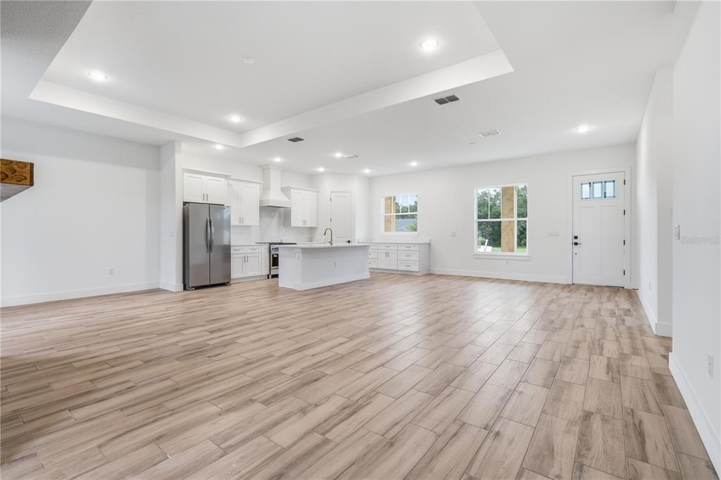 A bright, open-concept kitchen and living area features white cabinetry, stainless appliances, and wood-look flooring — 3890 SE 139 TERRACE, MORRISTON, FL