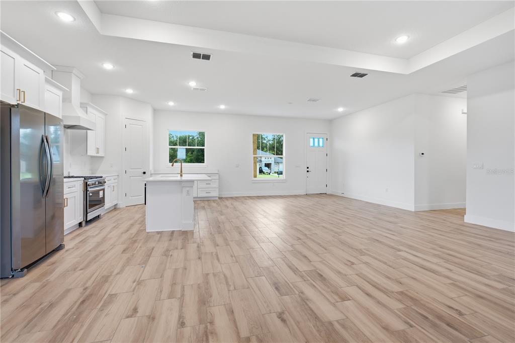 A bright, open-concept kitchen and living area features white cabinetry, stainless appliances, and wood-look flooring — 3890 SE 139 TERRACE, MORRISTON, FL