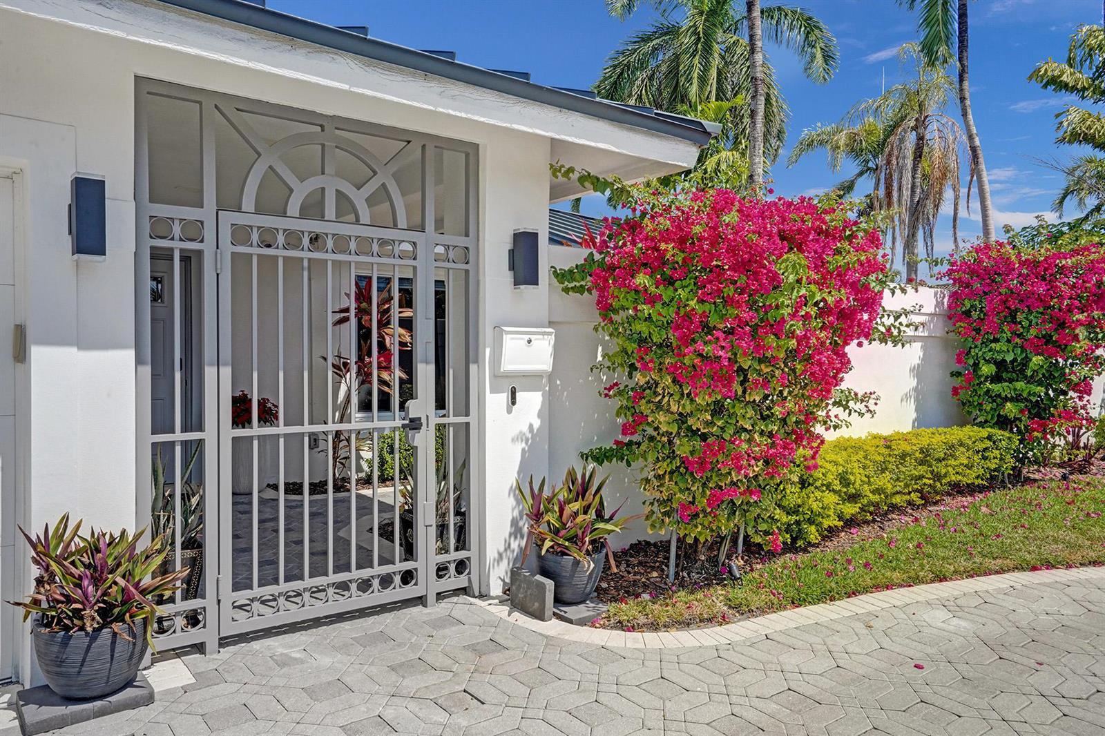 A white stucco wall with a gray metal gate and vibrant pink bougainvillea bushes — 201 SE 11th Street, Pompano Beach FL 33060, POMPANO BEACH, FL