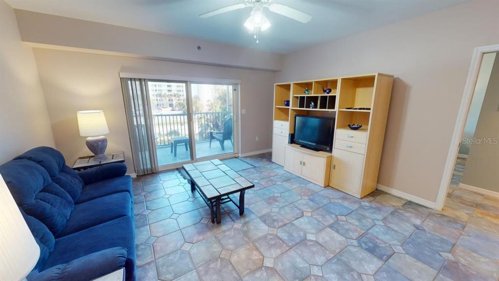 A living room features a blue sofa, tile flooring, a media center, and a balcony — 5300 S ATLANTIC AVENUE UNIT 23003, NEW SMYRNA BEACH, FL