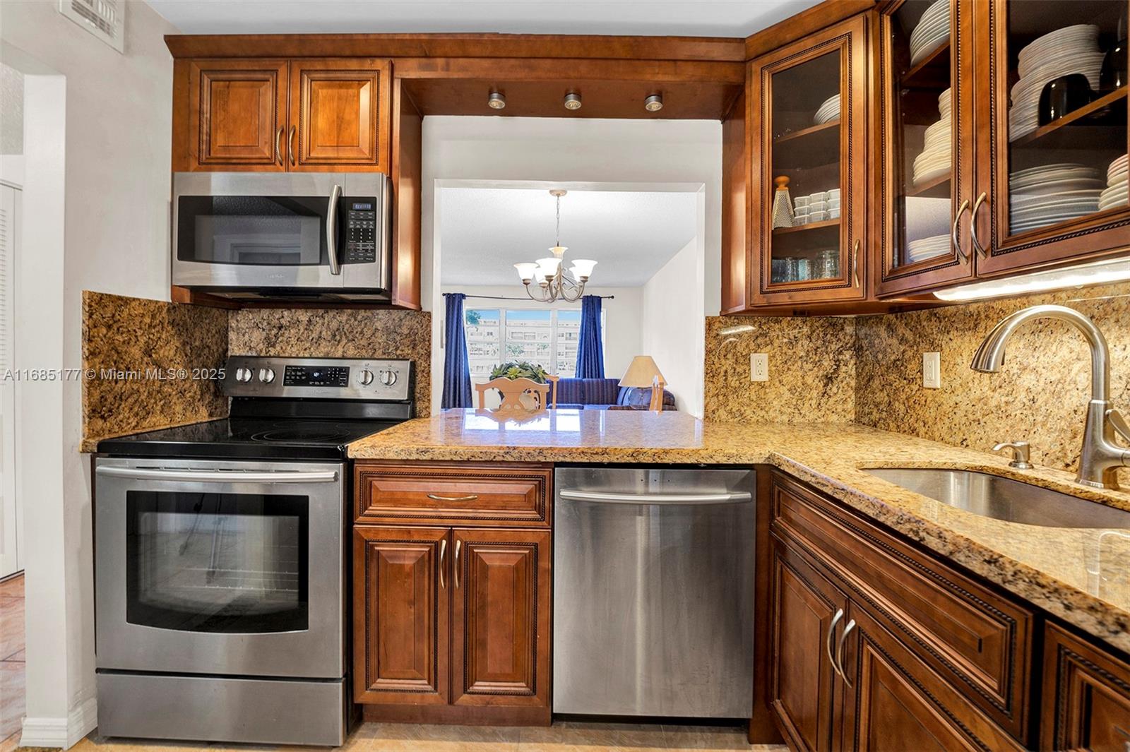A kitchen features wood cabinets, granite countertops, stainless steel appliances, and a view into a dining area — 410 SE 2nd St # 220, Hallandale Beach FL 33009, HALLANDALE BEACH, FL