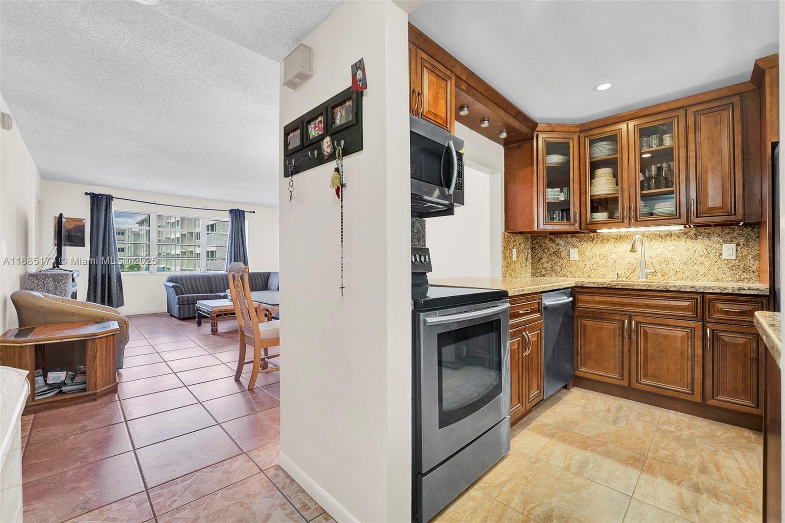 A kitchen with wood cabinets and granite countertops opens into a living area with tile floors — 410 SE 2nd St # 220, Hallandale Beach FL 33009, HALLANDALE BEACH, FL