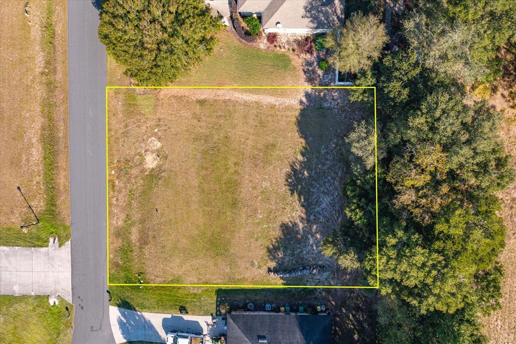 An aerial view shows a rectangular vacant residential lot outlined in yellow next to a road — 1103 MYRTLE BREEZES COURT, FRUITLAND PARK, FL
