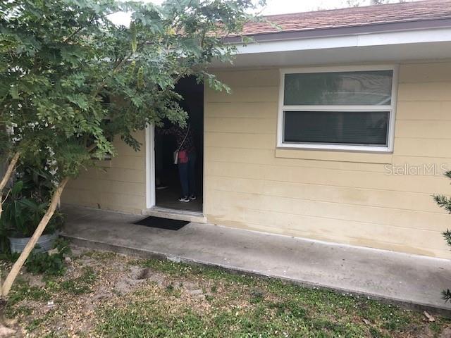 A light yellow house exterior features a concrete porch, a single window, and an open doorway — 7105 POINSETTA AVENUE UNIT 1, CAPE CANAVERAL, FL