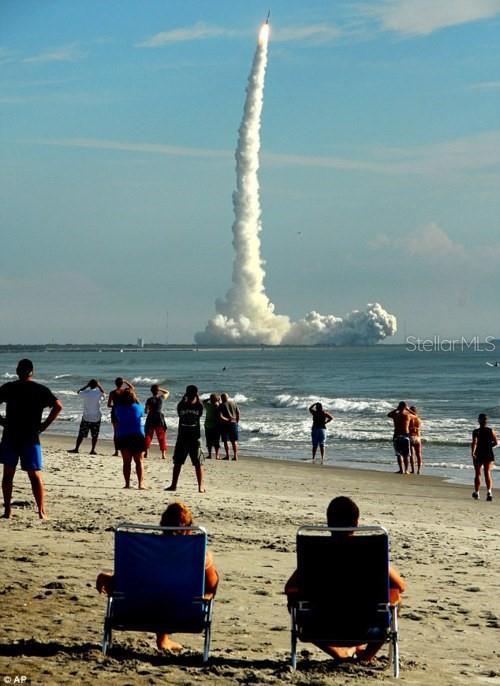 People on a sandy beach watch a rocket launch into the sky over the ocean — 7105 POINSETTA AVENUE UNIT 1, CAPE CANAVERAL, FL