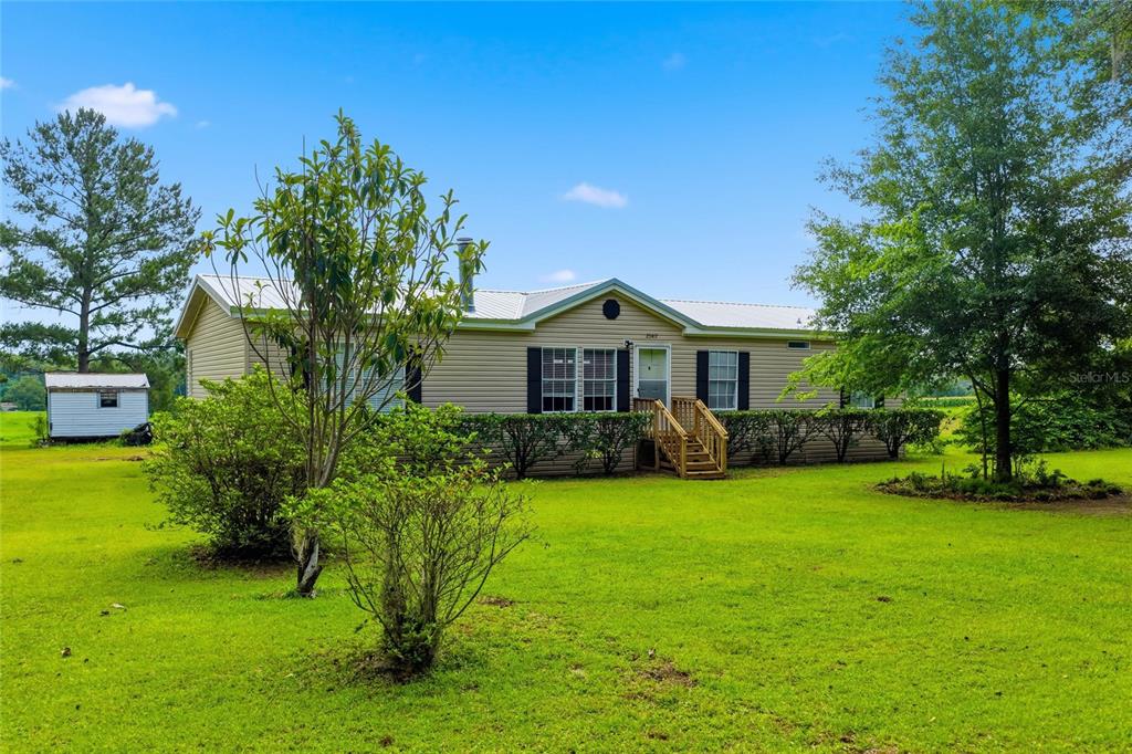 A single-story tan house with a metal roof sits on a large grassy lot — 25417 OLD BELLAMY ROAD, HIGH SPRINGS, FL
