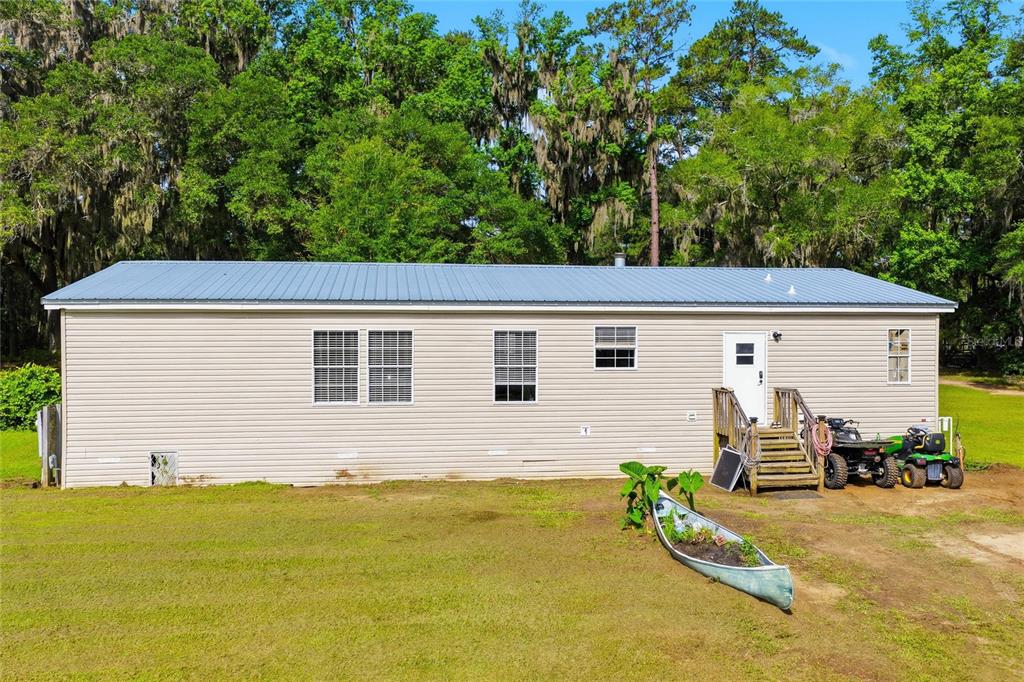 A single-story house with light siding, a metal roof, and a wooden deck entrance — 25417 OLD BELLAMY ROAD, HIGH SPRINGS, FL