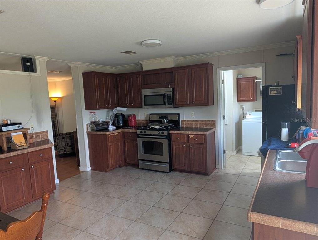 A kitchen features wood cabinets, stainless steel appliances, tile flooring, and an adjacent laundry room — 25417 OLD BELLAMY ROAD, HIGH SPRINGS, FL