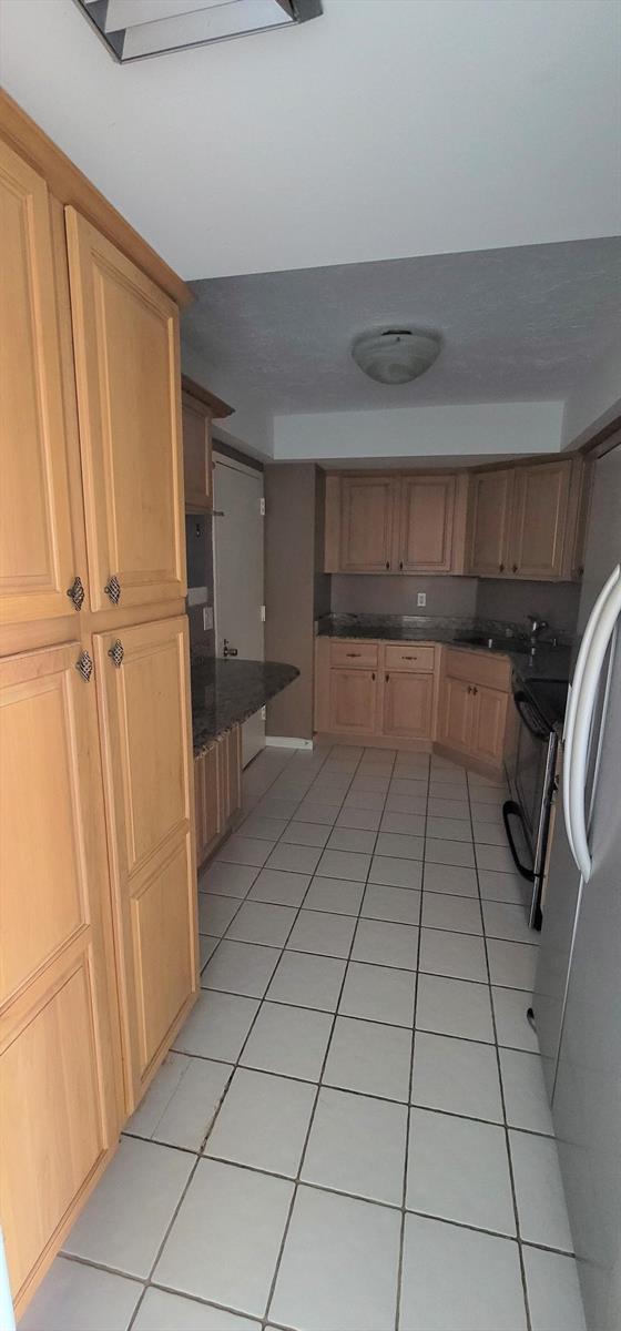 A kitchen features light wood cabinets, dark granite countertops, and white tiled flooring — 2425 Presidential Way # 402, West Palm Beach FL 33401, WEST PALM BEACH, FL