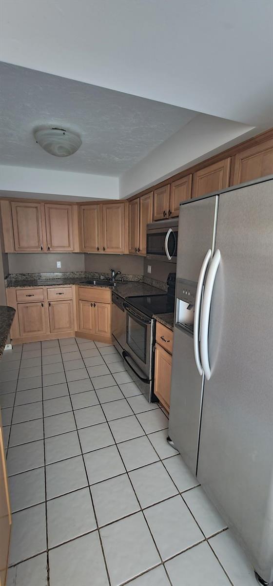 A kitchen features light wood cabinets, granite countertops, stainless steel appliances, and white tile flooring — 2425 Presidential Way # 402, West Palm Beach FL 33401, WEST PALM BEACH, FL