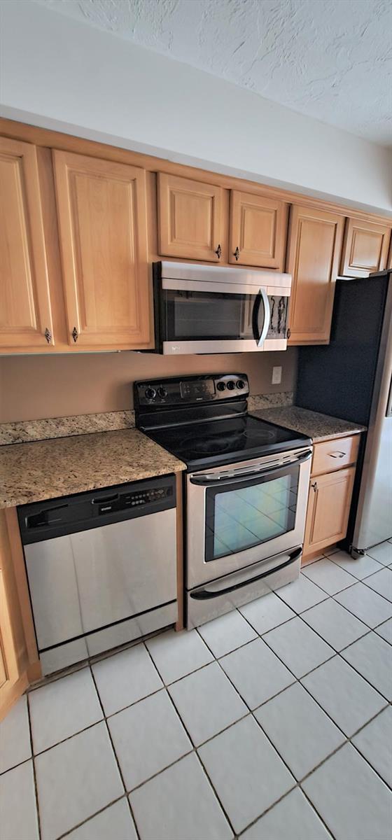 A kitchen features light wood cabinets, stainless steel appliances, granite countertops, and white tile flooring — 2425 Presidential Way # 402, West Palm Beach FL 33401, WEST PALM BEACH, FL