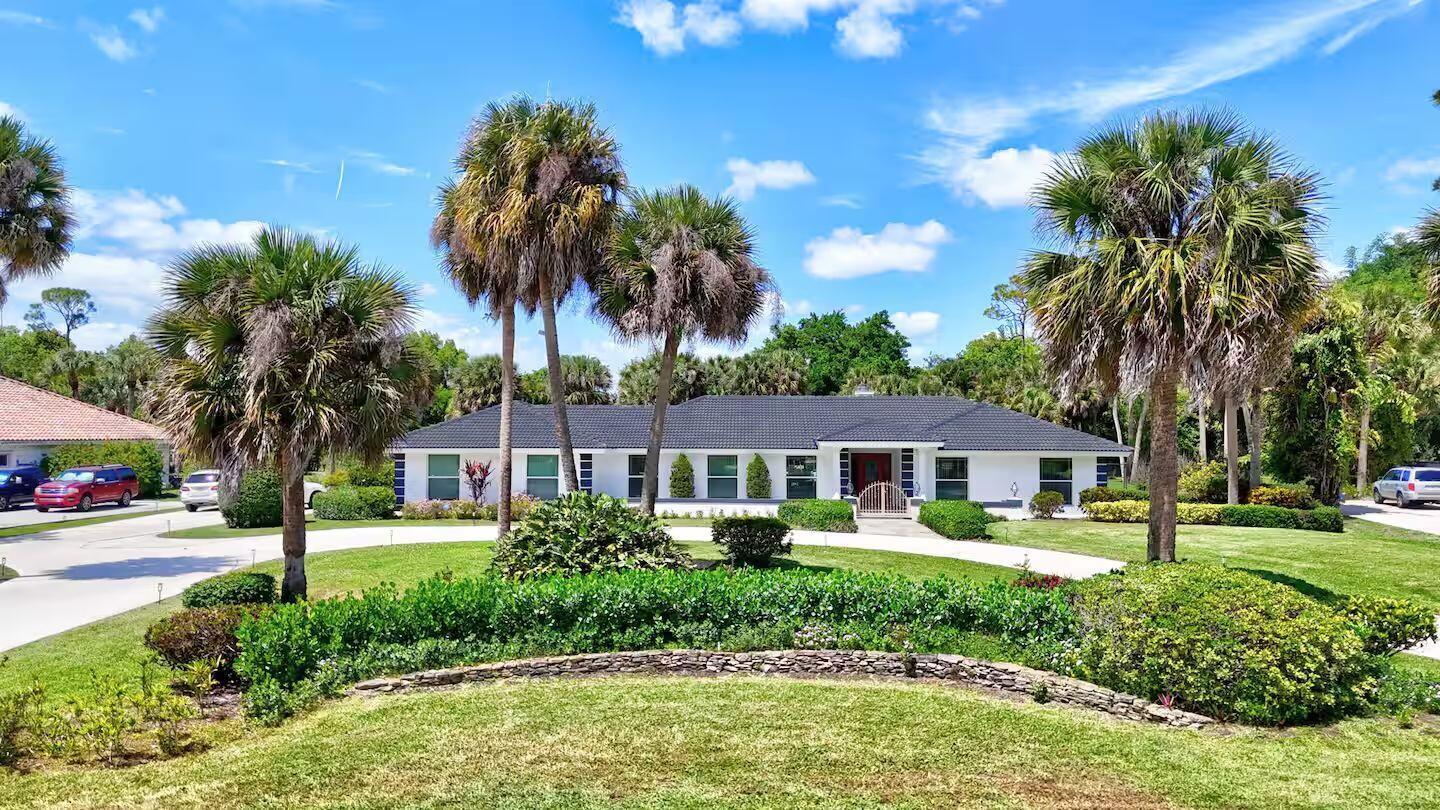 A single-story white house with a dark roof sits behind a landscaped lawn and palms — 12231 Areaca Drive, Wellington FL 33414, WELLINGTON, FL