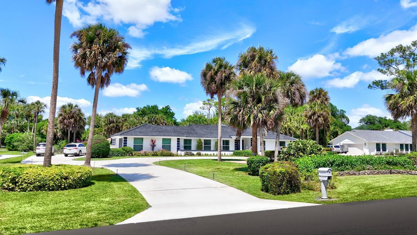 A white single-story house with a dark roof sits behind a long concrete driveway — 12231 Areaca Drive, Wellington FL 33414, WELLINGTON, FL