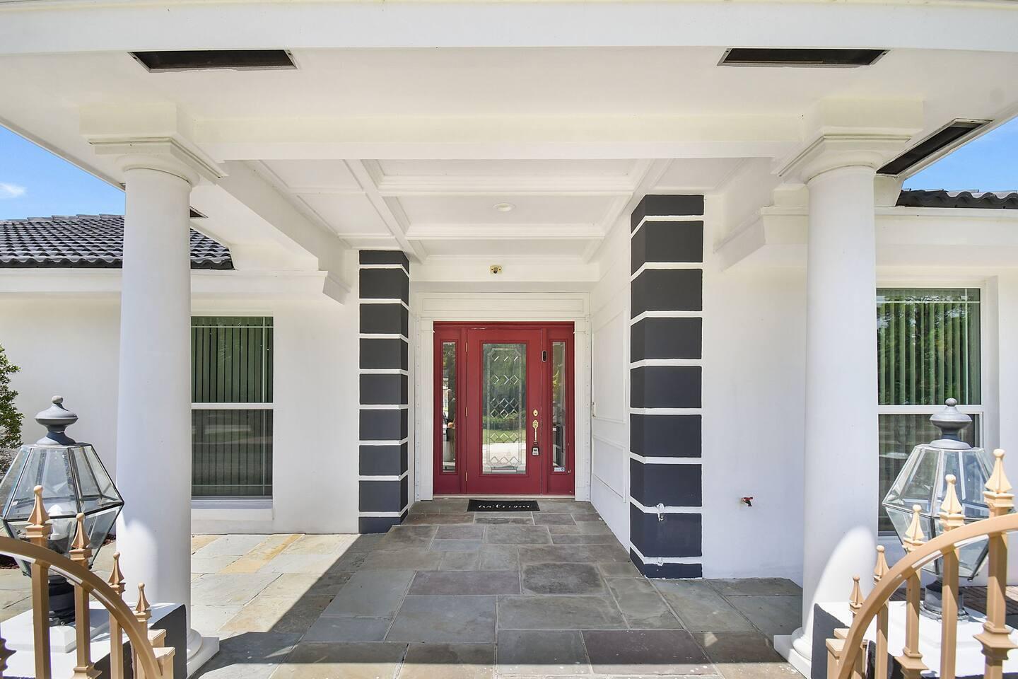 A covered entryway features a red front door, stone flooring, and two large white columns — 12231 Areaca Drive, Wellington FL 33414, WELLINGTON, FL