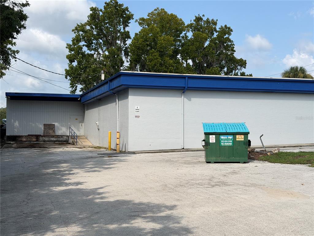 The exterior of a commercial building features a gray brick wall, blue trim, and a dumpster — 5920 SE HAMES ROAD, BELLEVIEW, FL