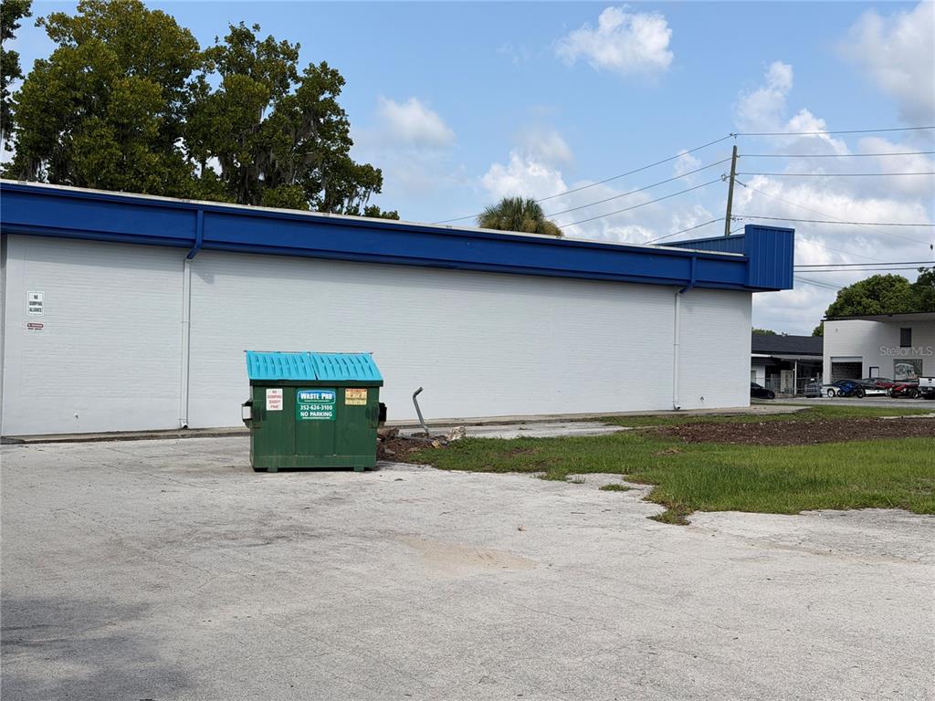 A green dumpster sits on a concrete lot in front of a white building — 5920 SE HAMES ROAD, BELLEVIEW, FL