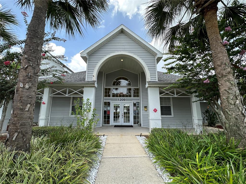A sidewalk leads to the entrance of a gray, single-story building with a peaked roof — 1218 BERMUDA LAKES LANE UNIT 203, KISSIMMEE, FL
