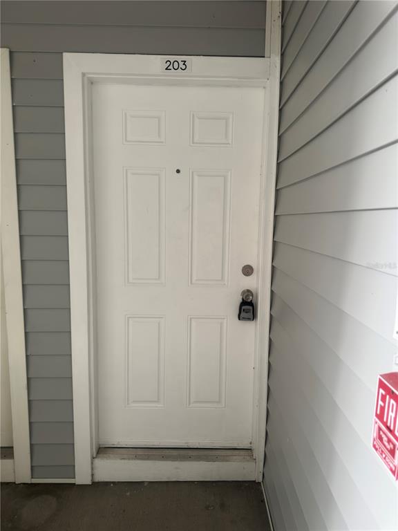 A white apartment door labeled 203 with a lockbox is set in gray siding — 1218 BERMUDA LAKES LANE UNIT 203, KISSIMMEE, FL