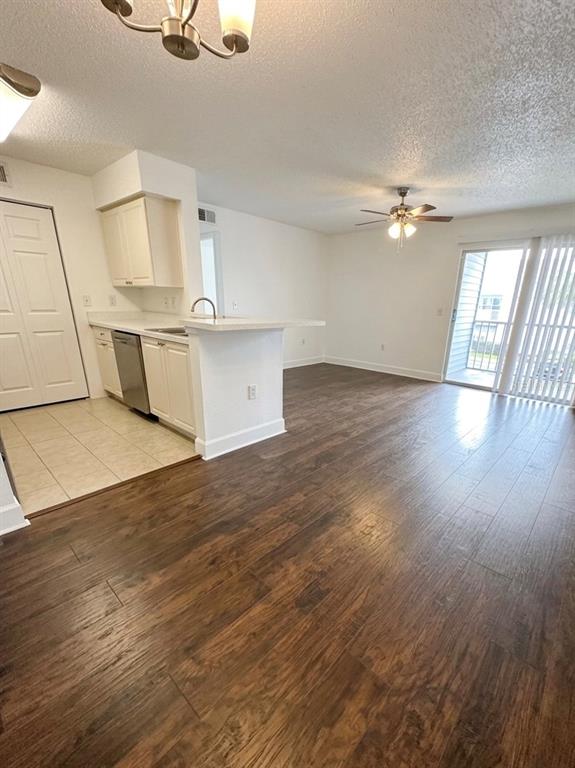 An open-concept living area features wood-look flooring, a kitchen with white cabinets, and balcony access — 1218 BERMUDA LAKES LANE UNIT 203, KISSIMMEE, FL