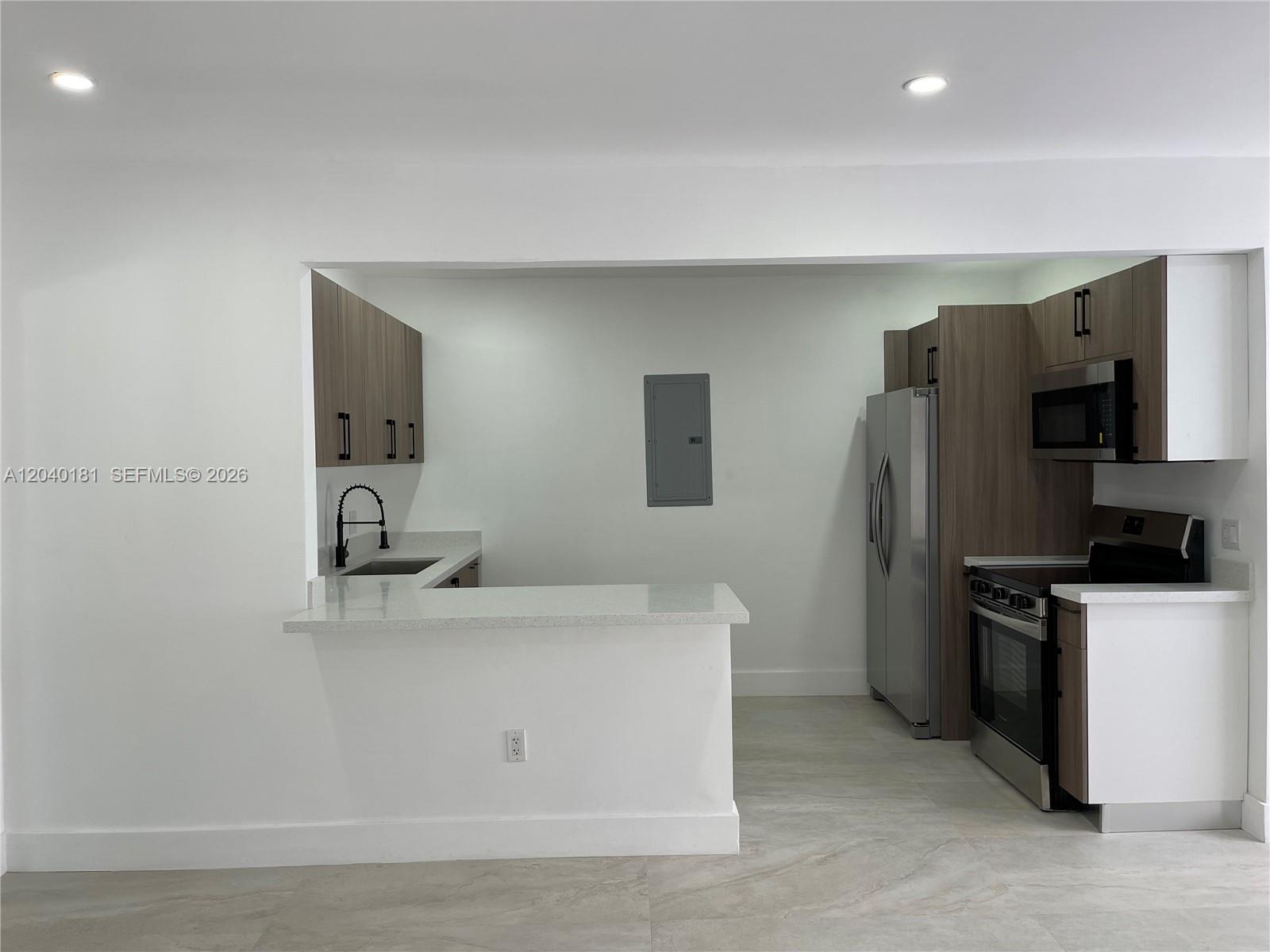 A modern kitchen features wood-tone cabinets, stainless steel appliances, and a white quartz breakfast bar — 1310 Sharazad Blvd, Opa-Locka FL 33054, OPA-LOCKA, FL