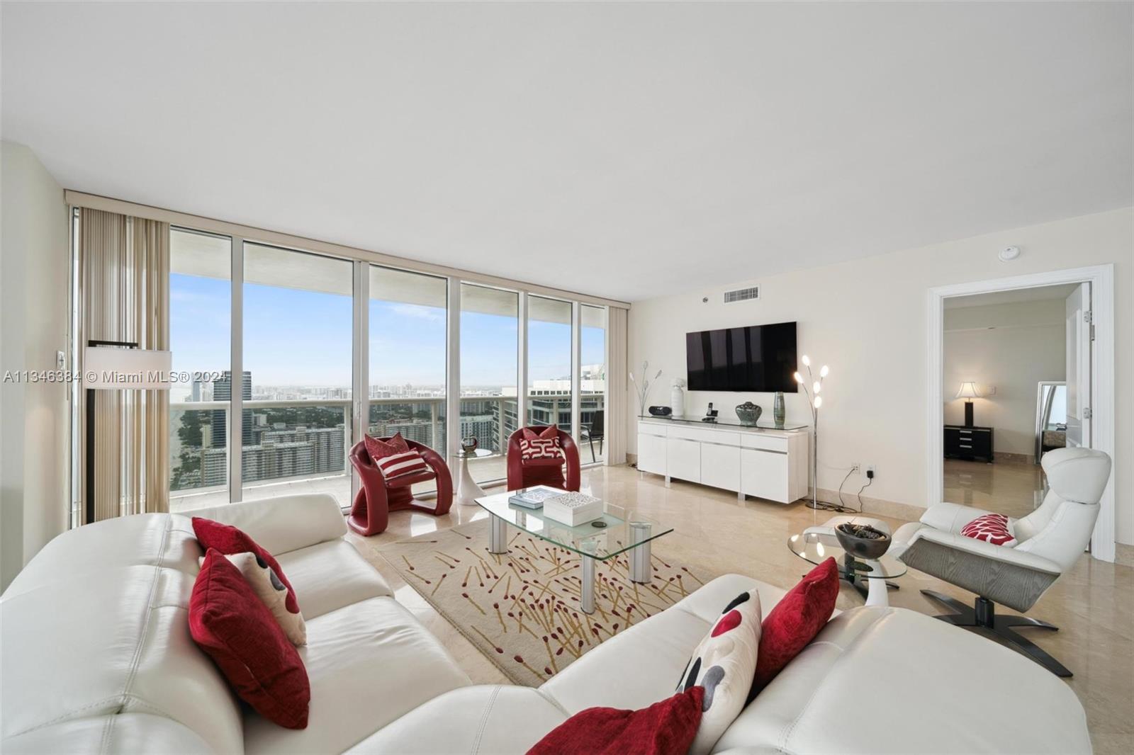 A bright living room features white leather sofas, red accent pillows, and floor-to-ceiling windows — 1830 S Ocean Dr # 4602, Hallandale Beach FL 33009, HALLANDALE BEACH, FL