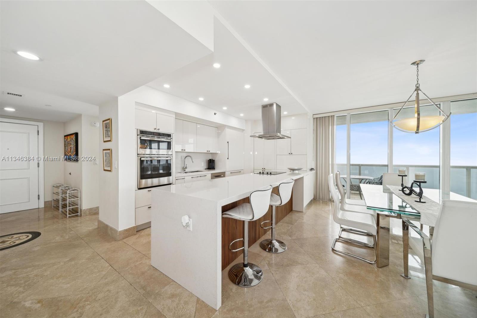 A modern kitchen features white cabinetry, a quartz island with bar stools, and tile flooring — 1830 S Ocean Dr # 4602, Hallandale Beach FL 33009, HALLANDALE BEACH, FL