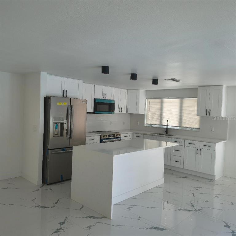 A modern kitchen features white cabinets, a central island, stainless steel appliances, and marble flooring — 7019 FOUNTAIN AVENUE, TAMPA, FL