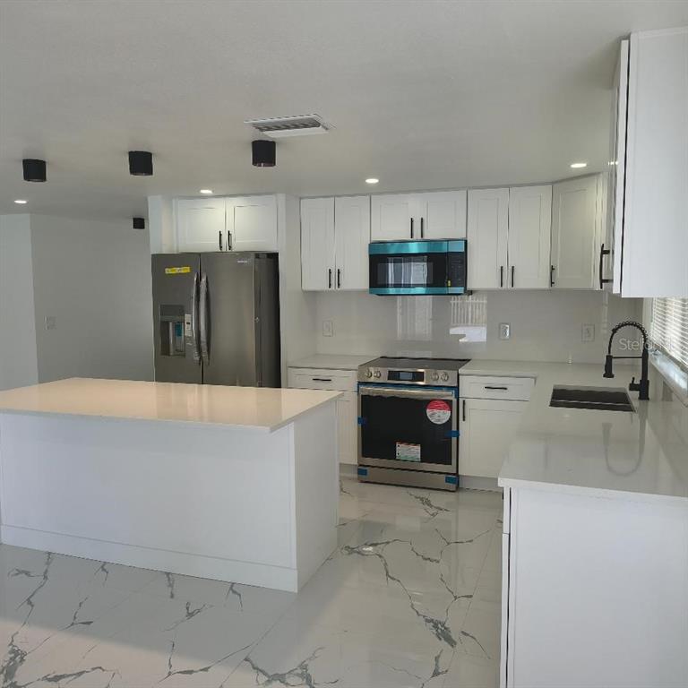 A modern kitchen features white cabinets, stainless steel appliances, a center island, and marble-patterned flooring — 7019 FOUNTAIN AVENUE, TAMPA, FL