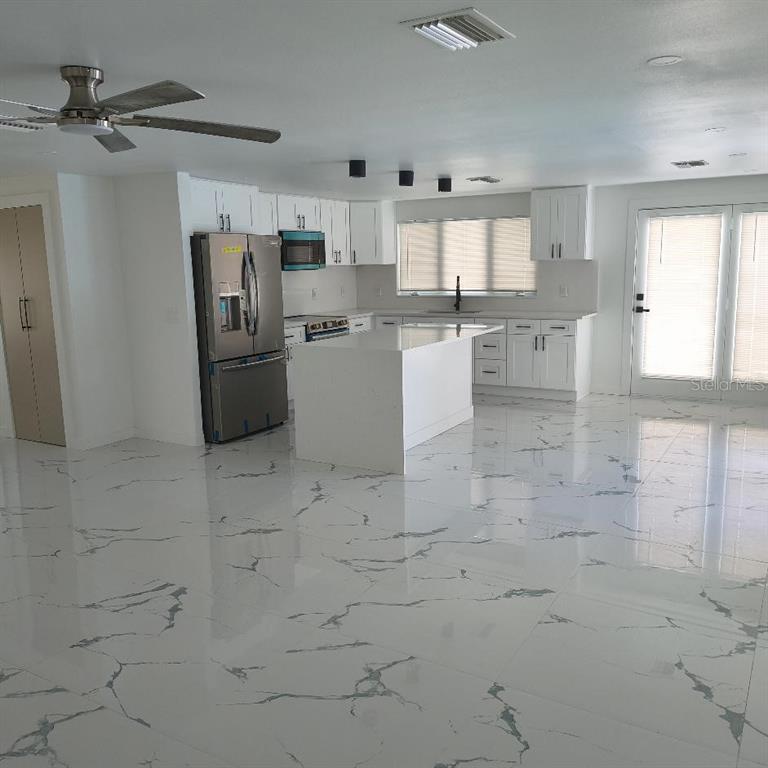 A modern kitchen features white cabinetry, a central island, and white marble-patterned tile flooring — 7019 FOUNTAIN AVENUE, TAMPA, FL