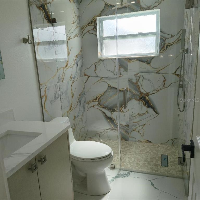 A bathroom features a glass-enclosed shower with marble-patterned tile walls and a white vanity — 7019 FOUNTAIN AVENUE, TAMPA, FL