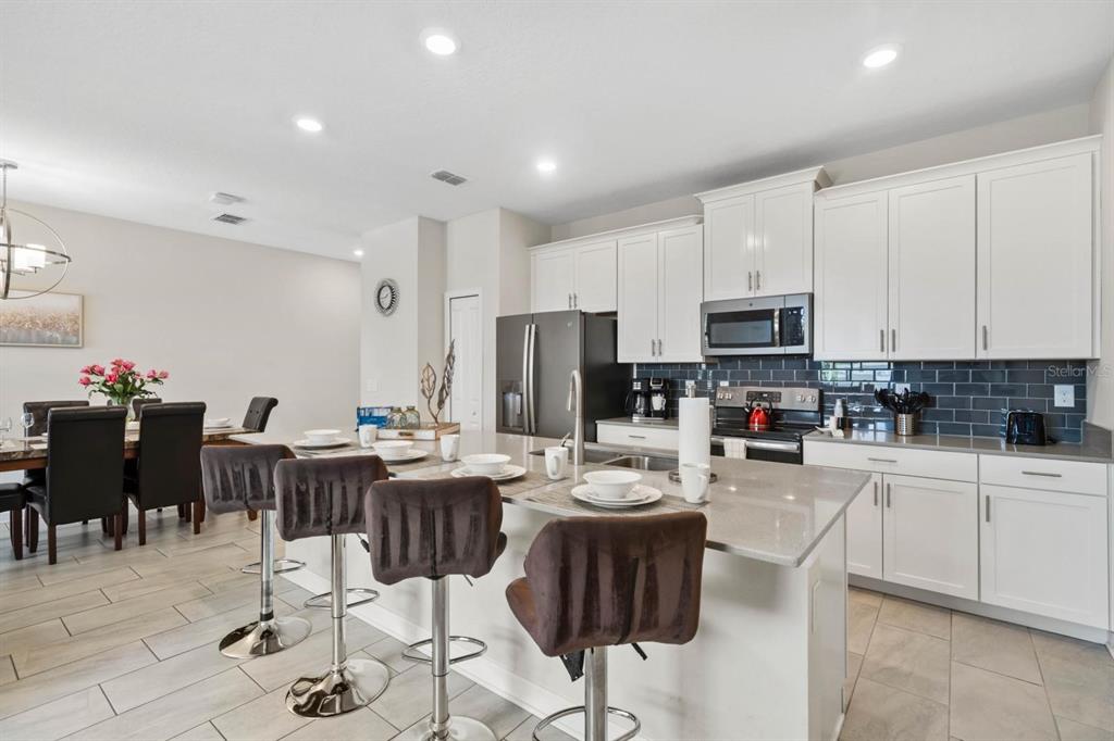 A kitchen with white cabinets, a gray island, and bar stools next to a dining area — 900 PEBBLE BEACH DRIVE, DAVENPORT, FL