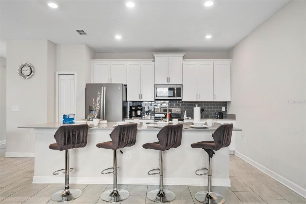 A kitchen with white cabinets, a gray tiled backsplash, and a breakfast bar with four stools — 900 PEBBLE BEACH DRIVE, DAVENPORT, FL