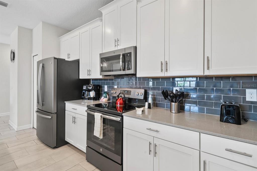 A kitchen features white cabinets, gray subway tile backsplash, quartz countertops, and black appliances — 900 PEBBLE BEACH DRIVE, DAVENPORT, FL