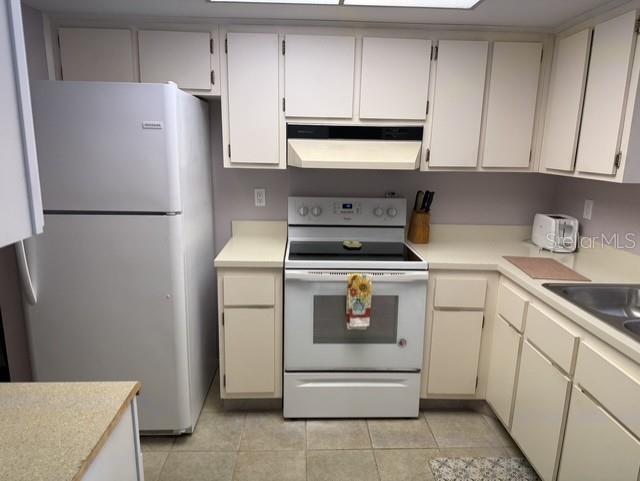 A kitchen features white cabinets, a white refrigerator, a white electric range, and beige countertops — 1100 EAST BAY DRIVE UNIT 89, LARGO, FL