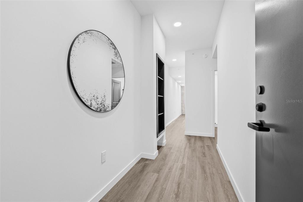 A bright, modern hallway features light wood-look flooring, white walls, and a round wall mirror — 221 MAIN STREET N UNIT B1-1013, ST PETERSBURG, FL