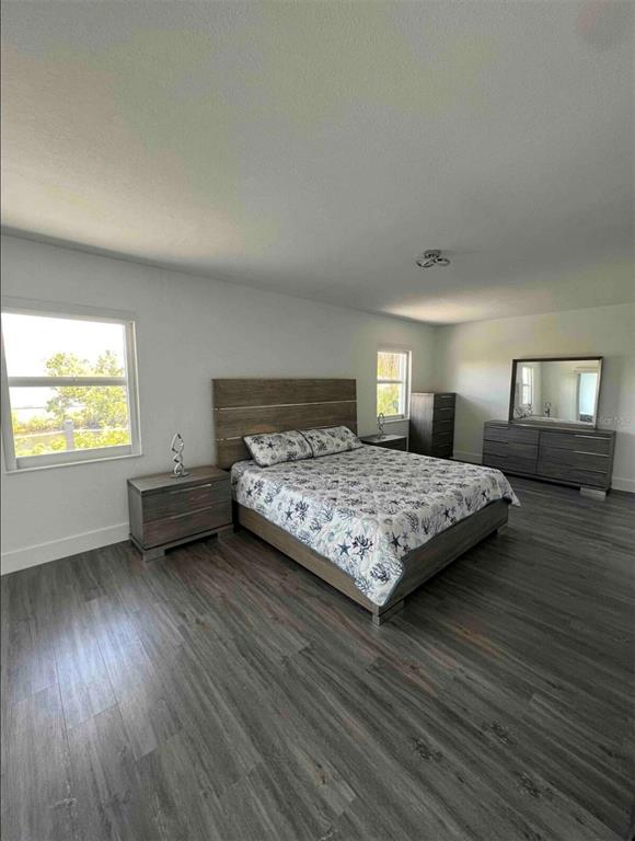A bedroom features a bed, dresser, nightstands, and wood-look flooring with two windows overlooking greenery — 3004 BANYAN WAY, PUNTA GORDA, FL