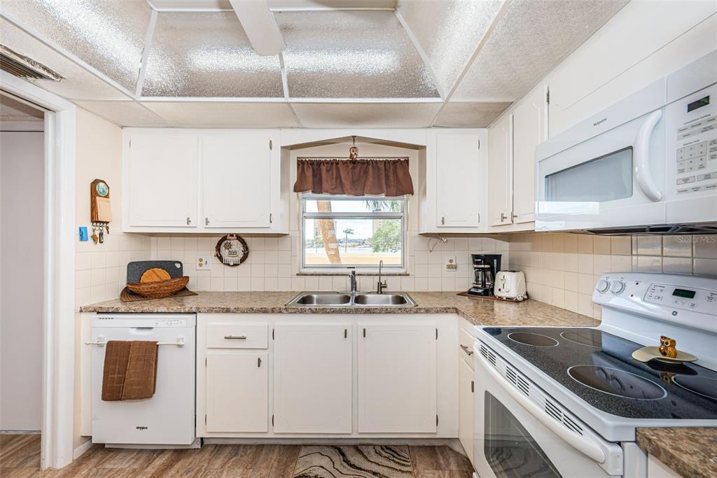 A kitchen features white cabinets, a double sink, a glass-top stove, and a window view — 4725 COVE CIRCLE UNIT 210, ST PETERSBURG, FL