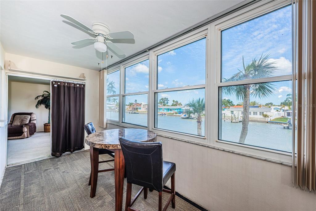 A sunroom features a dining table, a ceiling fan, and large windows overlooking a canal — 4725 COVE CIRCLE UNIT 210, ST PETERSBURG, FL