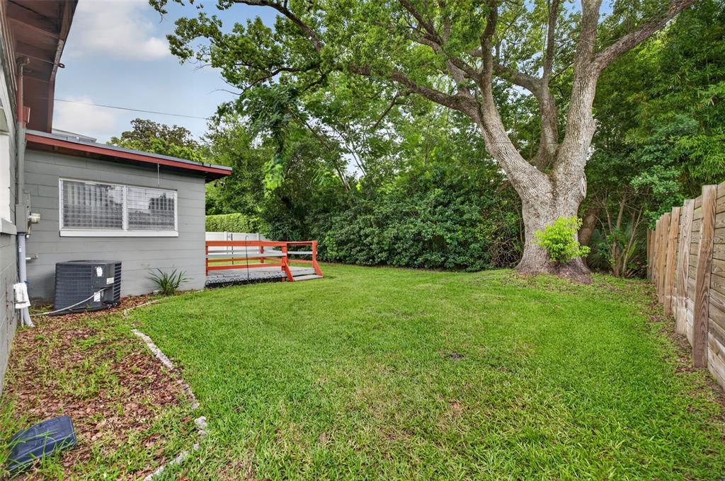 A grassy backyard features a large tree, a wooden fence, and a small red deck — 1622 ARBOR PARK DRIVE, WINTER PARK, FL