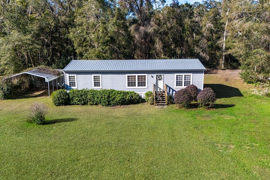 A single-story manufactured home with a metal roof, carport, and front steps sits on grass — 21800 SW 15TH AVENUE, NEWBERRY, FL