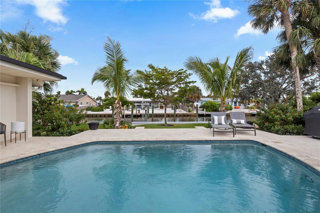 A swimming pool sits on a stone patio overlooking a canal with palm trees — 624 DUNDEE LANE, BRADENTON BEACH, FL
