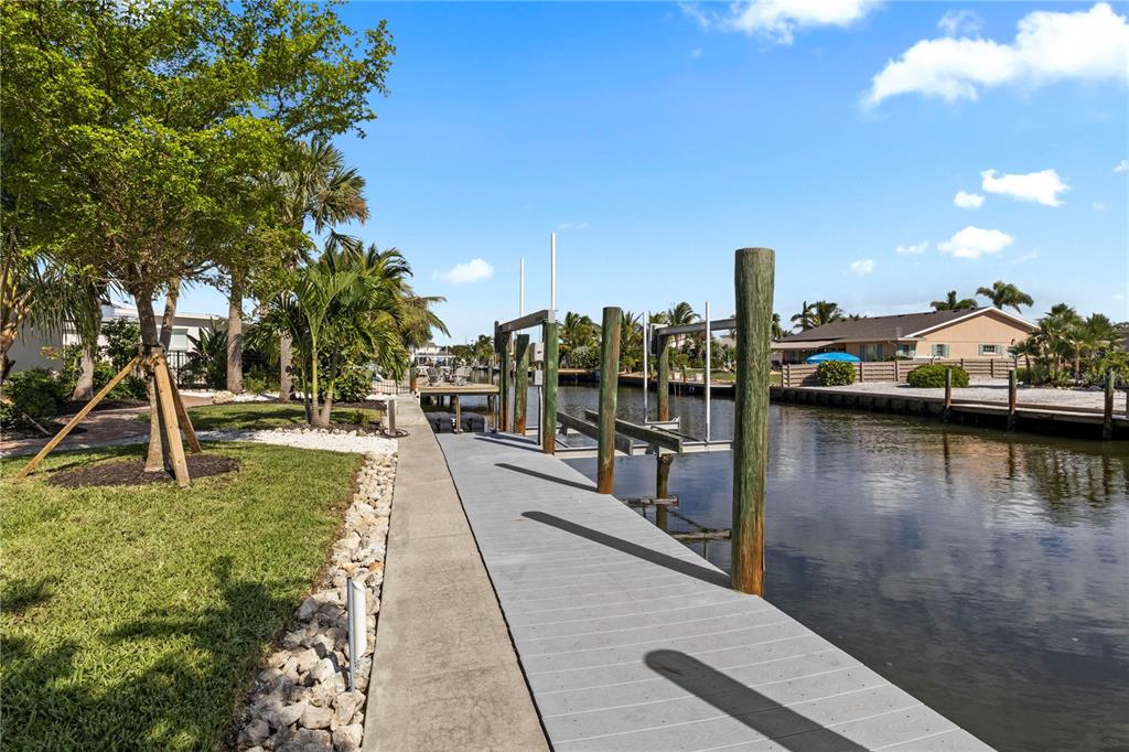 A concrete walkway leads to a wooden boat dock along a residential canal — 624 DUNDEE LANE, BRADENTON BEACH, FL