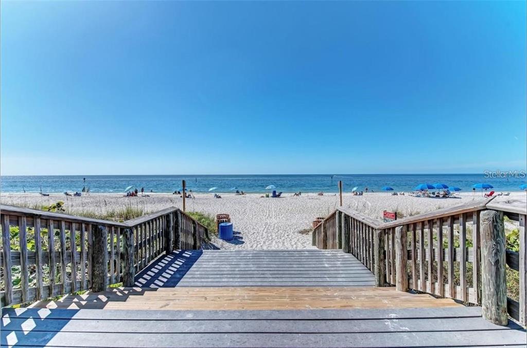 A wooden staircase leads down to a sandy beach with blue umbrellas under a clear sky — 12 PETUNIA COURT, PLACIDA, FL