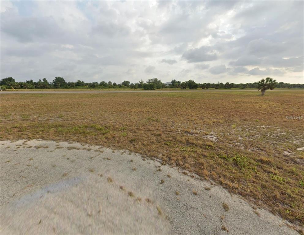 A wide, grassy vacant lot stretches toward a distant road under a cloudy sky — 12 PETUNIA COURT, PLACIDA, FL
