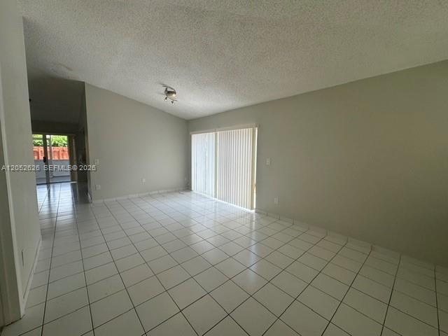 An empty room with white tile floors, a vaulted ceiling, and sliding glass patio doors — 13073 SW 150th Ter, Miami FL 33186, MIAMI, FL