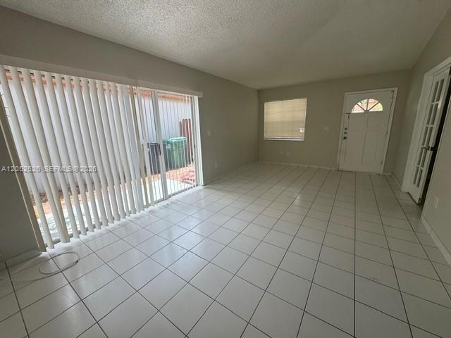 An empty living room features white tile flooring, a sliding glass door, and a front door — 13073 SW 150th Ter, Miami FL 33186, MIAMI, FL