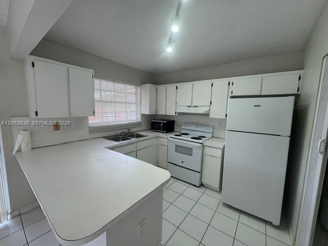 A kitchen features white cabinets, white appliances, a peninsula countertop, and white tiled flooring — 13073 SW 150th Ter, Miami FL 33186, MIAMI, FL