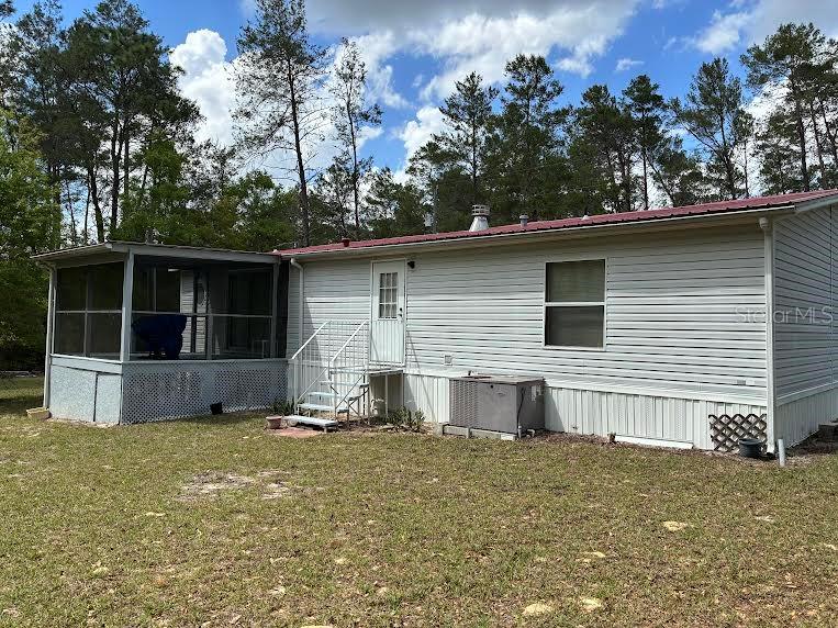 The exterior of a light-colored mobile home features a screened-in porch and a metal roof — 109 GREENWOOD ROAD, FLORAHOME, FL